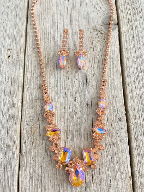 Rose gold-tone crystal statement necklace and matching iridescent drop earrings on pale weathered wood