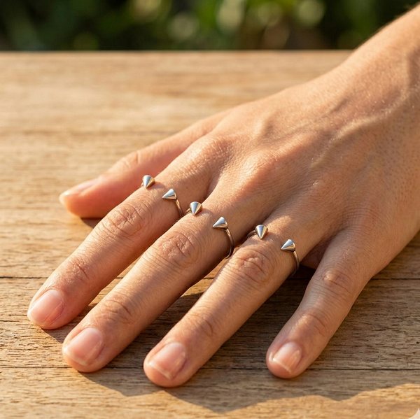 Hand wearing multiple small silver rings on a wooden surface
