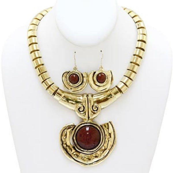Gold-tone statement necklace and matching drop earrings with oval dark red gemstone centers, displayed on a white jewelry bust.