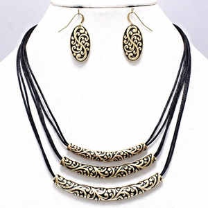 A jewelry set featuring a multi-strand black cord necklace with ornate gold filigree cylindrical and oval beads, paired with matching oval drop earrings on a white display bust.