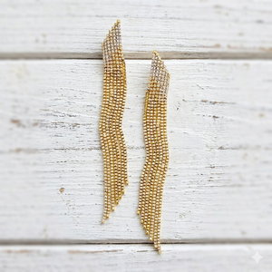 Gold beaded statement earrings on a light wooden surface
