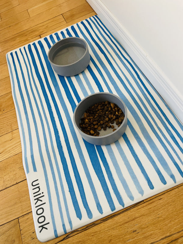 Striped mat with two gray bowls on a wooden floor, featuring the brand 'uniklook'.