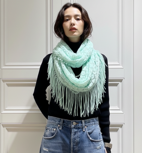 Person wearing a light blue scarf with white fringe in front of a white paneled wall.