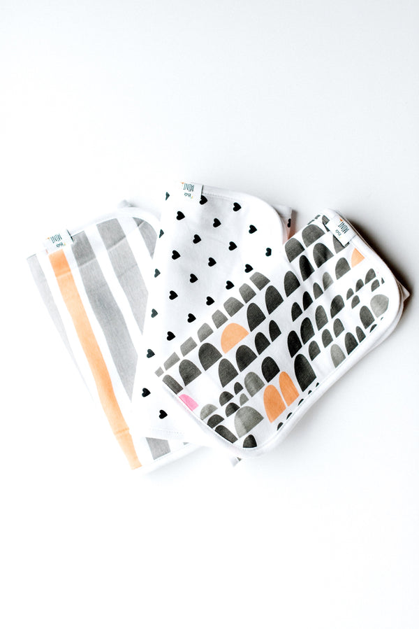 A folded white and patterned burp cloth with geometric designs on a white background