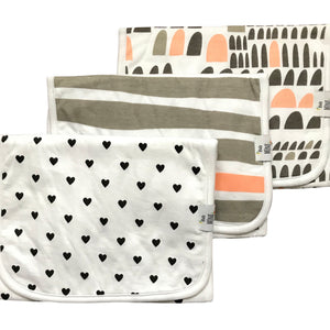 Three burp cloths with various patterns, including hearts, solid color, and geometric designs, displayed side by side.