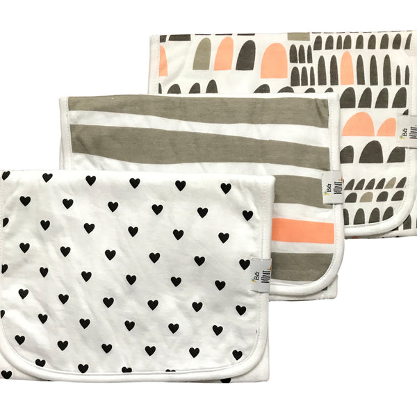Three burp cloths with various patterns, including hearts, solid color, and geometric designs, displayed side by side.